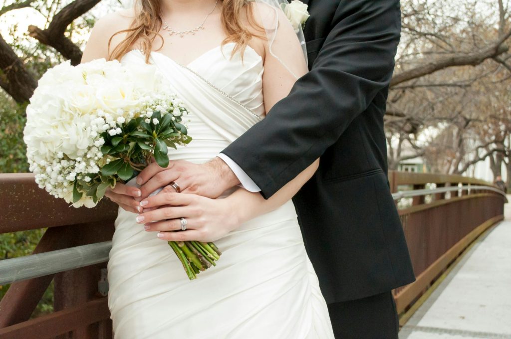 Bride and groom embracing outdoors holding a bouquet, symbolizing romance and love.