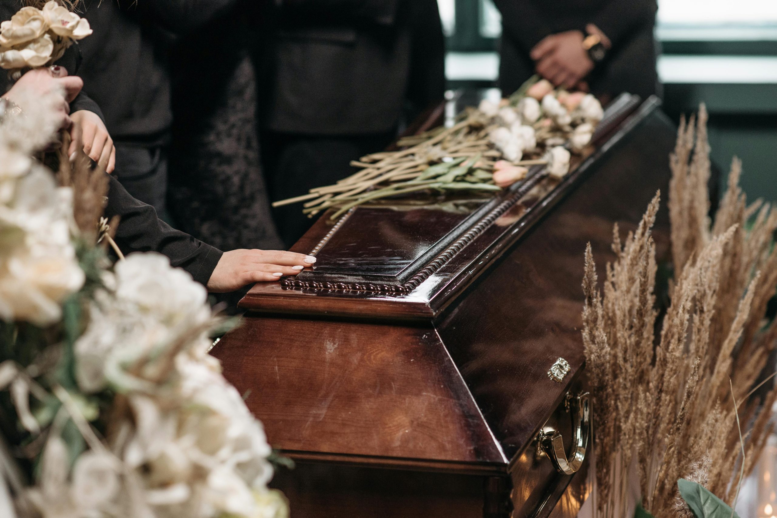A poignant funeral moment with mourners gathered around a coffin decorated with flowers.