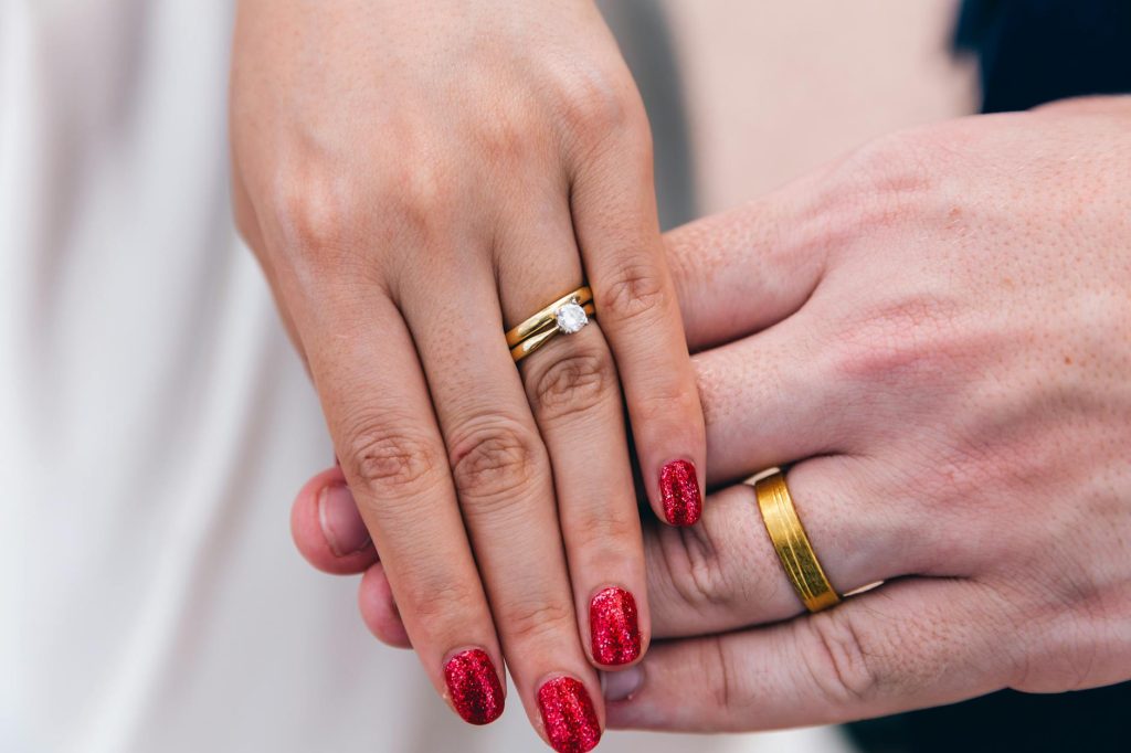 A close-up photo of a couple's hands showing wedding and engagement rings.